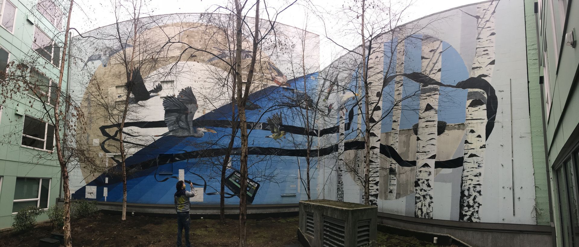 Large mural on building with blue and white abstract shapes; trees in foreground.