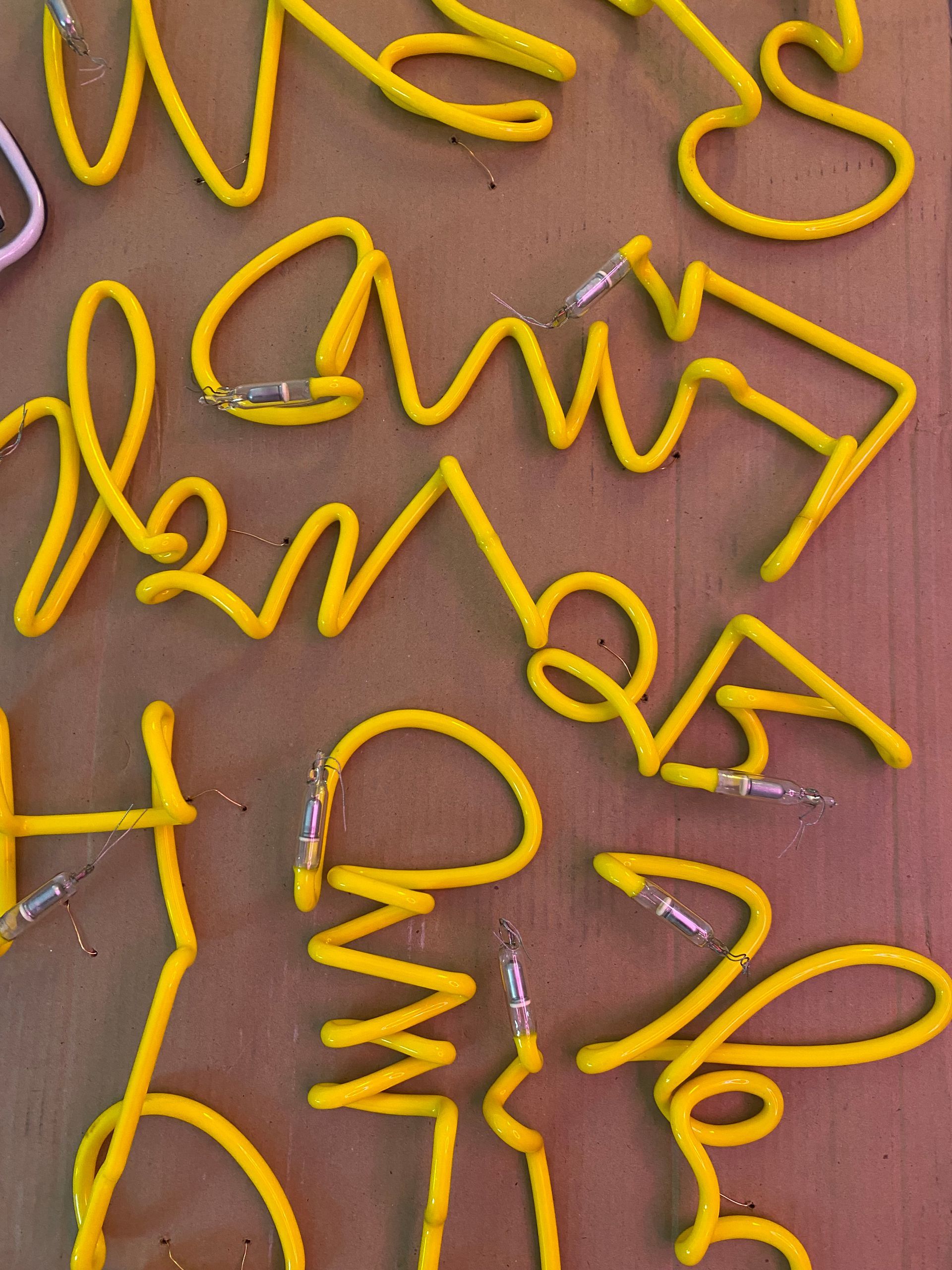 A curved length of light yellow neon tubing by Yale Wolf rests on a workbench, positioned above a sketched design on paper.