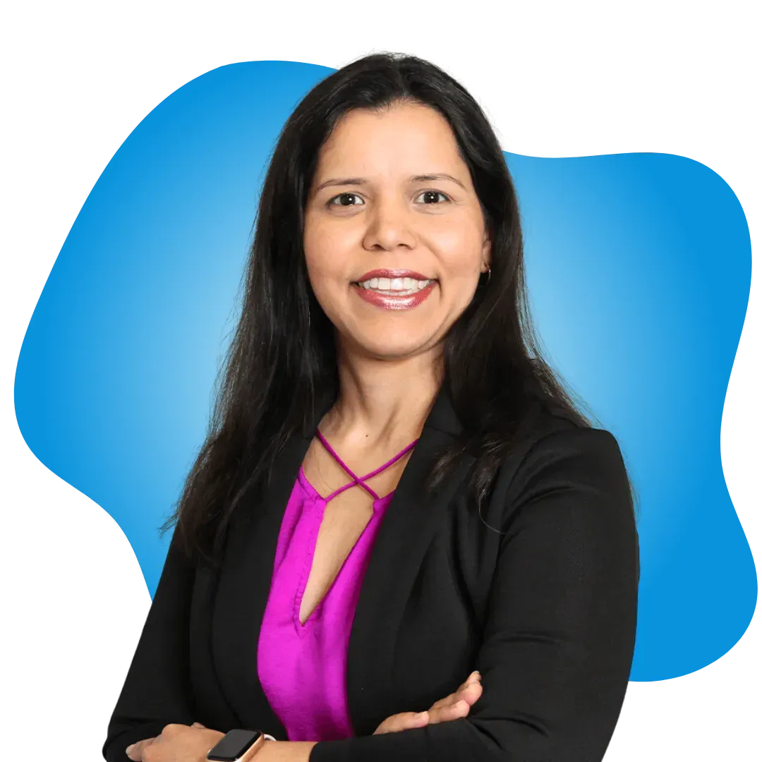 A woman wearing a black jacket and a pink shirt is smiling with her arms crossed.