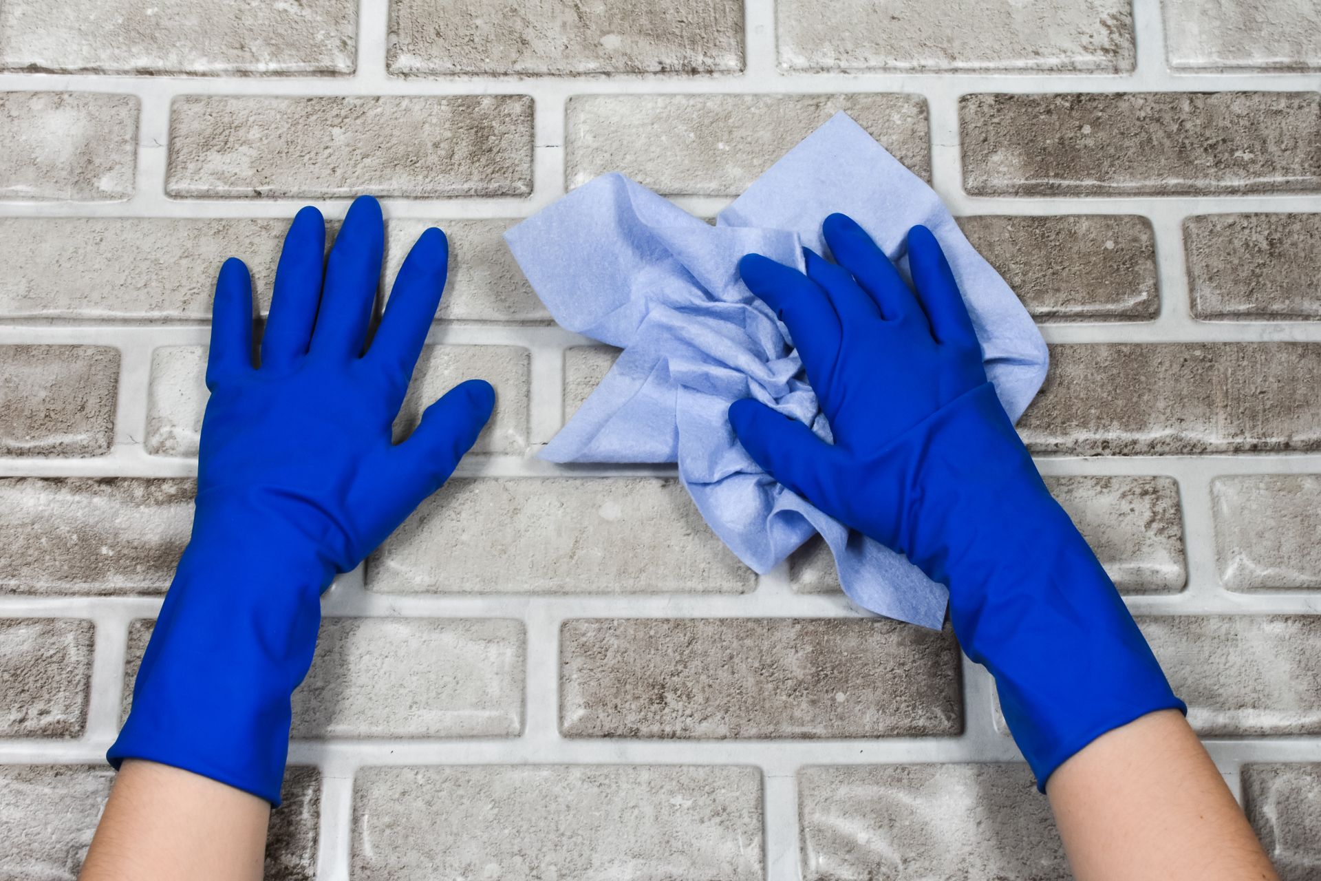 Blue-gloved hands cleaning a brick wall with a white cloth