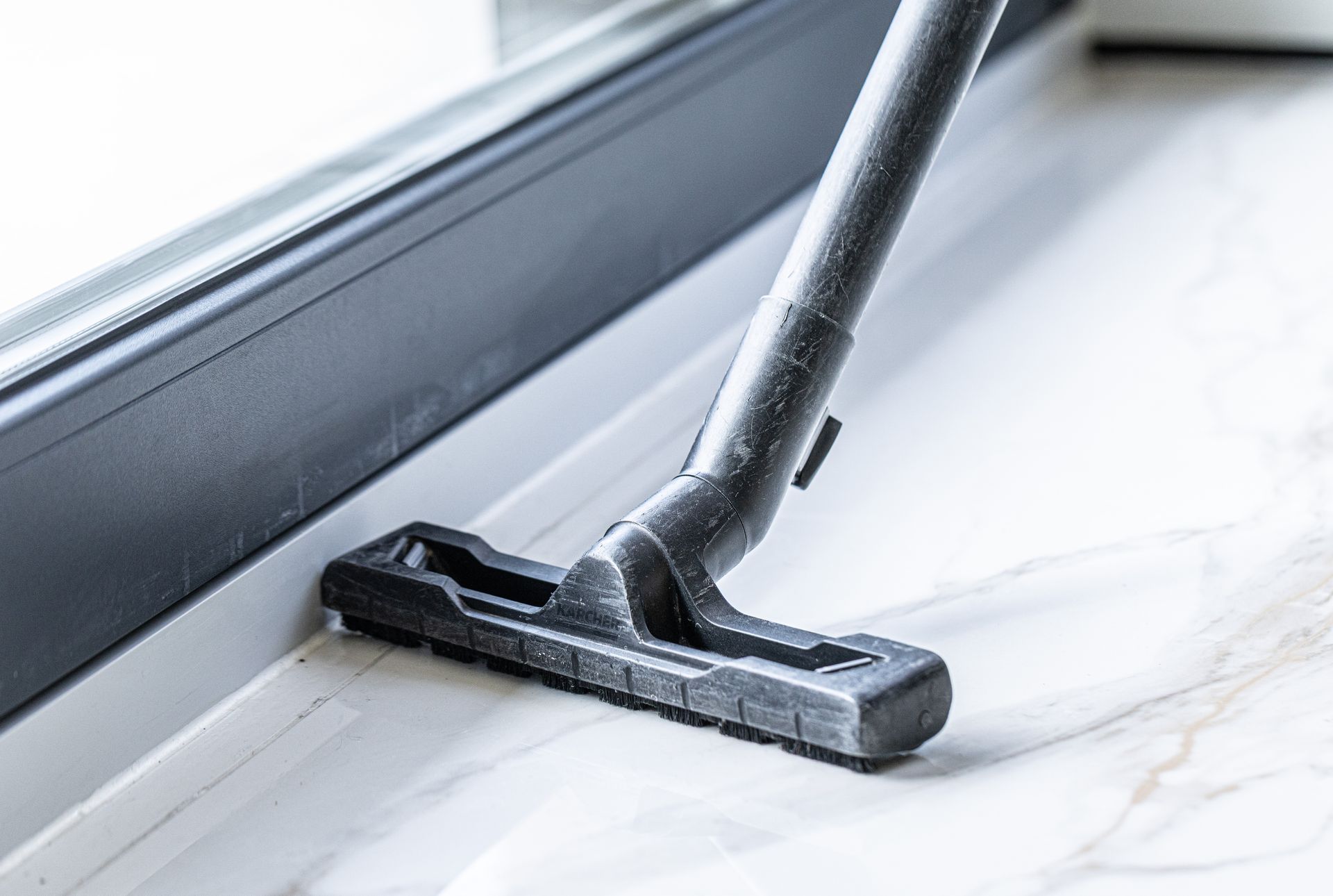 Vacuum cleaner nozzle on a white floor beside a window sill