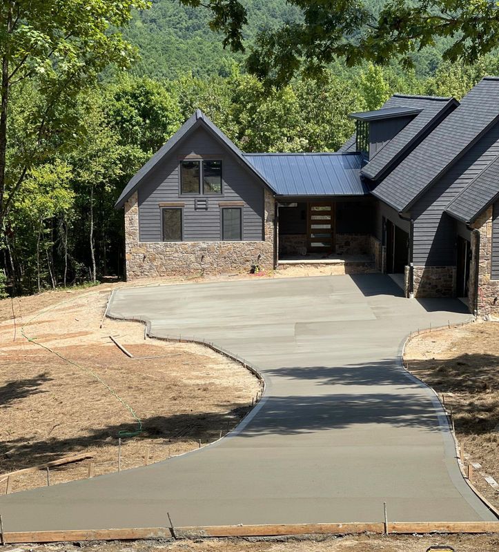 A large house with a concrete driveway leading to it is surrounded by trees.