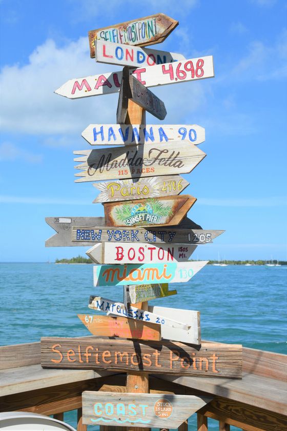 Wooden signpost with multiple directions. Destinations include London, Havana, and Boston; a blue ocean and sky backdrop.