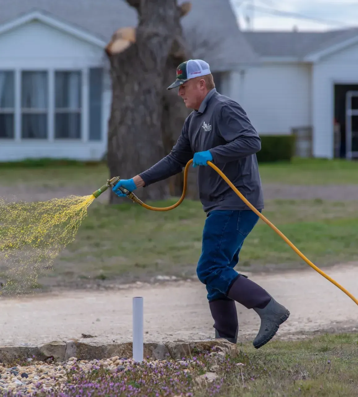A man is spraying flowers with a hose in front of a house