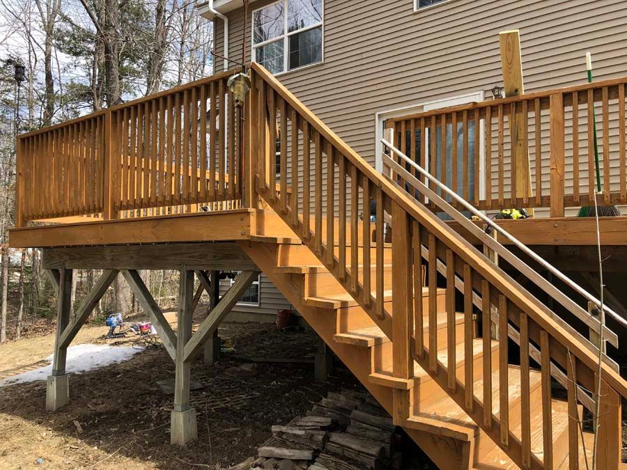 A wooden deck with stairs leading up to it and a house in the background.