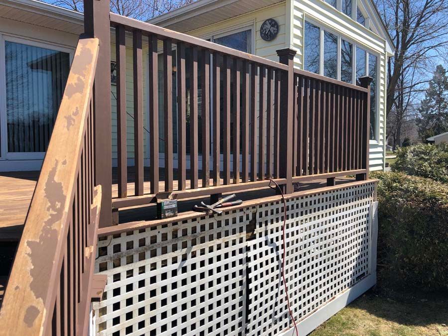 A deck with a brown railing and a white lattice fence in front of a house.