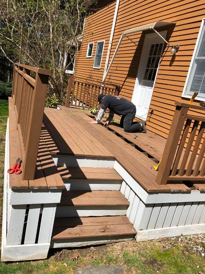 A man is working on a wooden deck in front of a house.