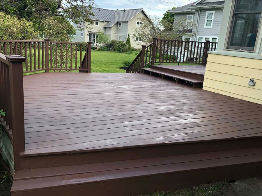 A large wooden deck with stairs and a railing in front of a house.
