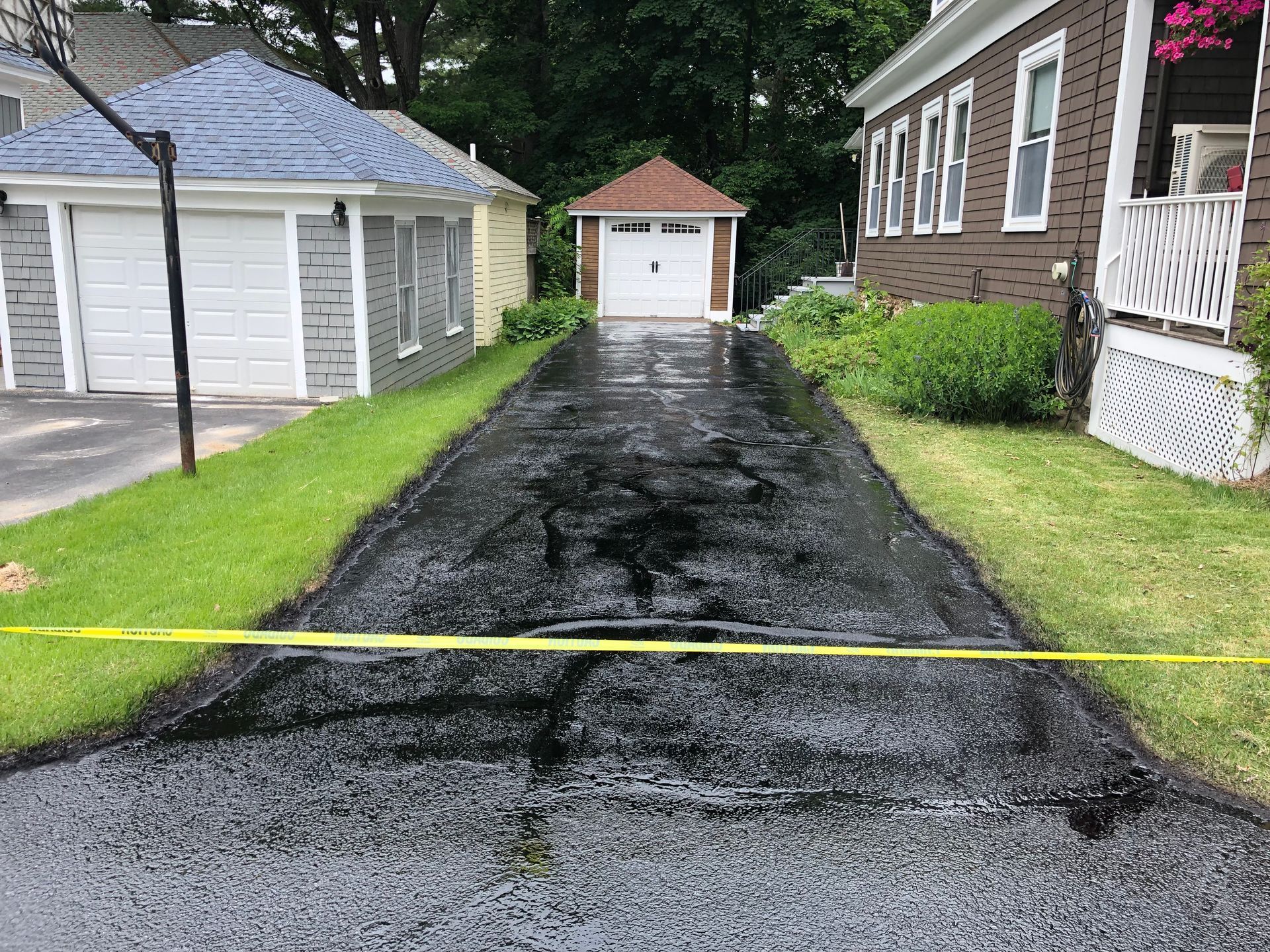 A black asphalt driveway leading to a house with a yellow tape.