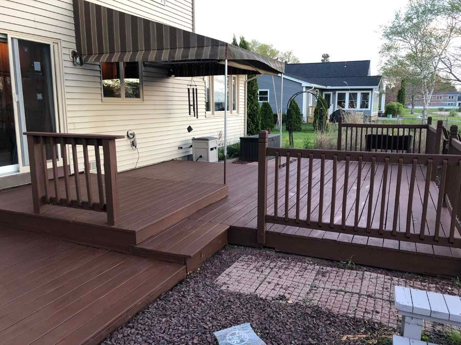 A wooden deck with a striped awning is in front of a house.