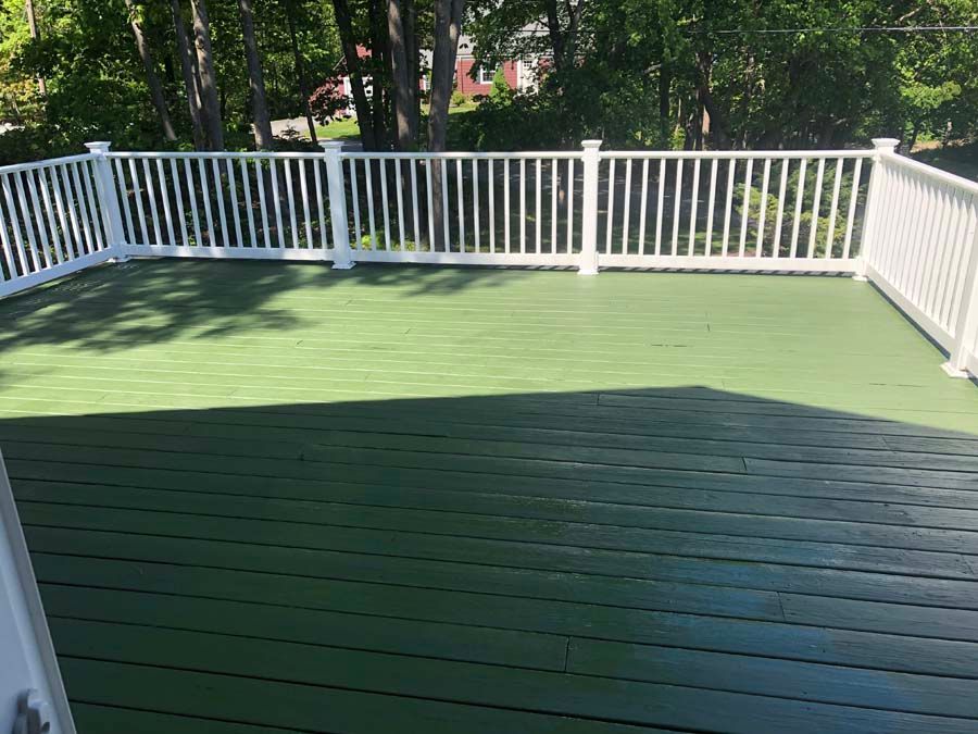 A green deck with a white railing and trees in the background.