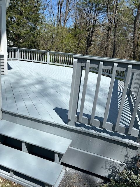 A green deck with a white railing and trees in the background.