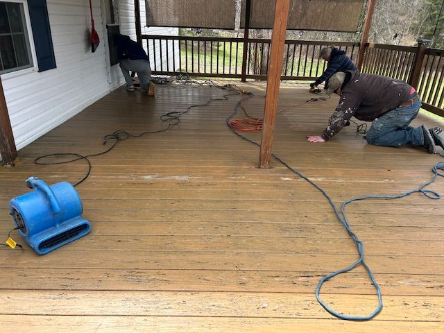 Workers pressure-washing a wooden porch deck with hoses and a blue blower
