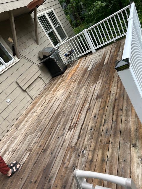 A man is cleaning a wooden deck with a sprayer.