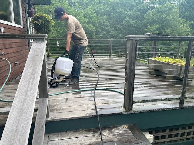A man is cleaning a wooden deck with a sprayer.
