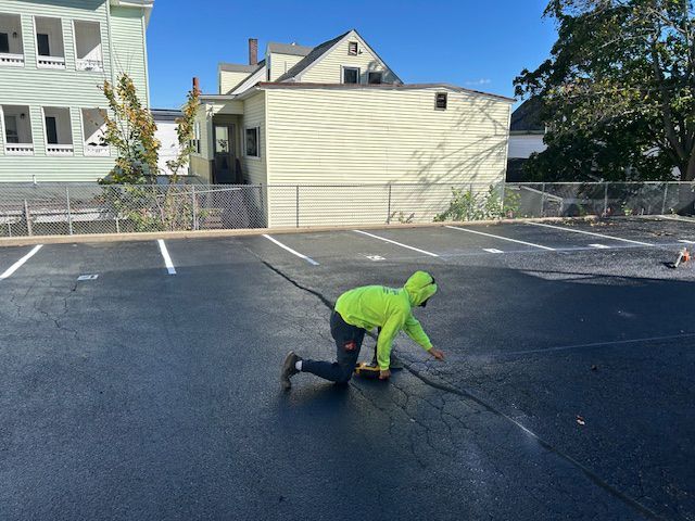 Person in neon green hoodie on hands and knees examining a crack in a newly paved parking lot.
