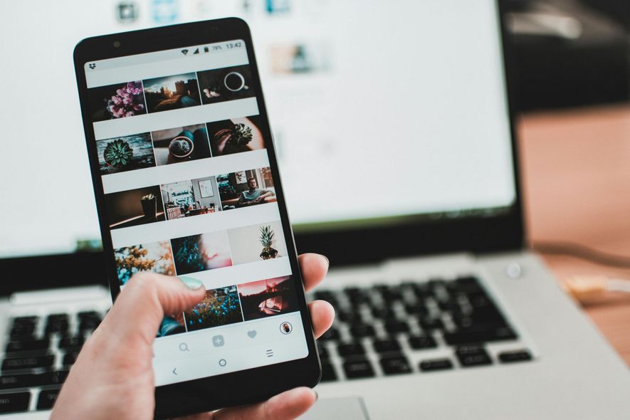 A person is holding a cell phone in front of a laptop.