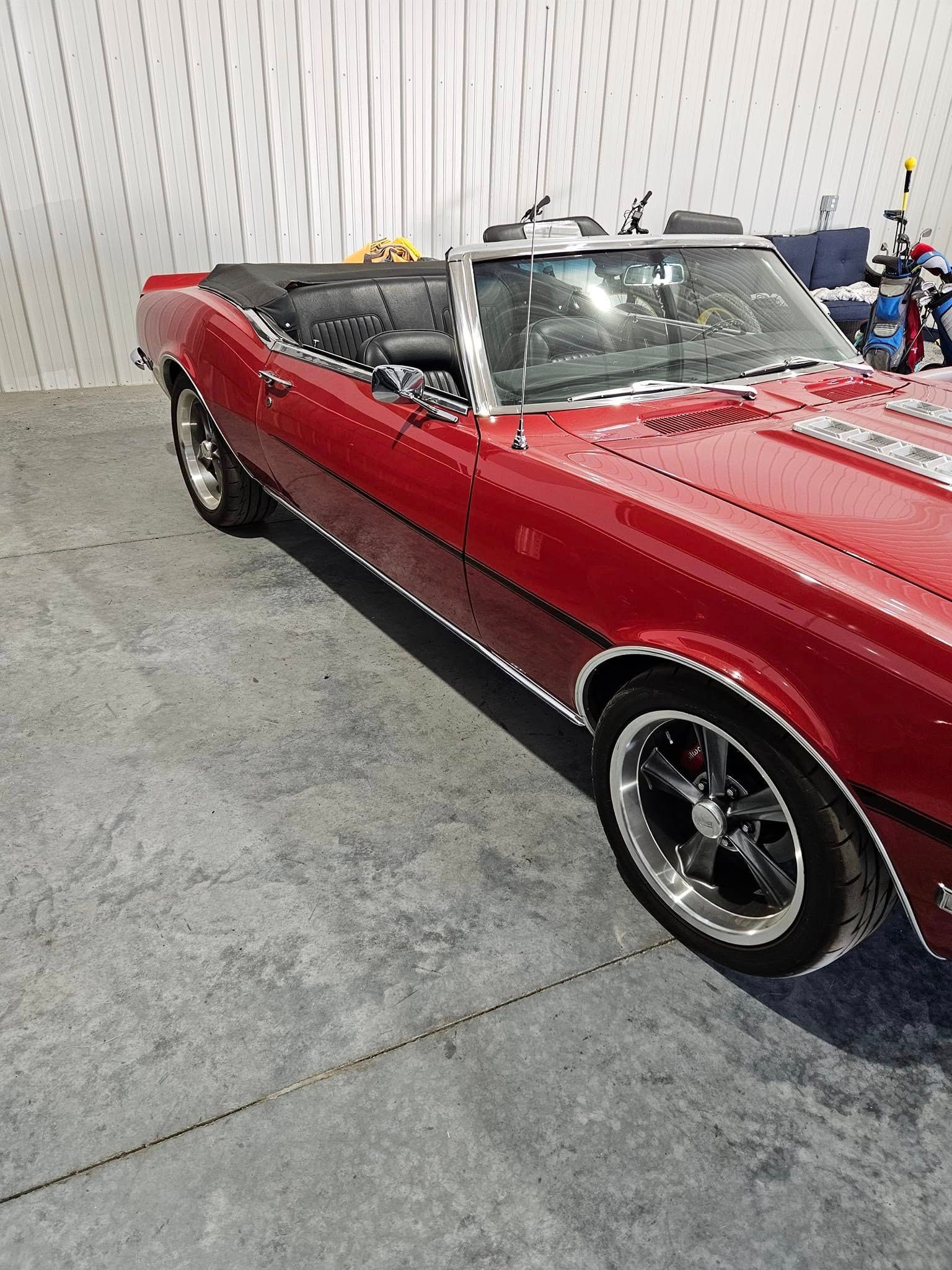 A red convertible classic car parked on a paved lot.