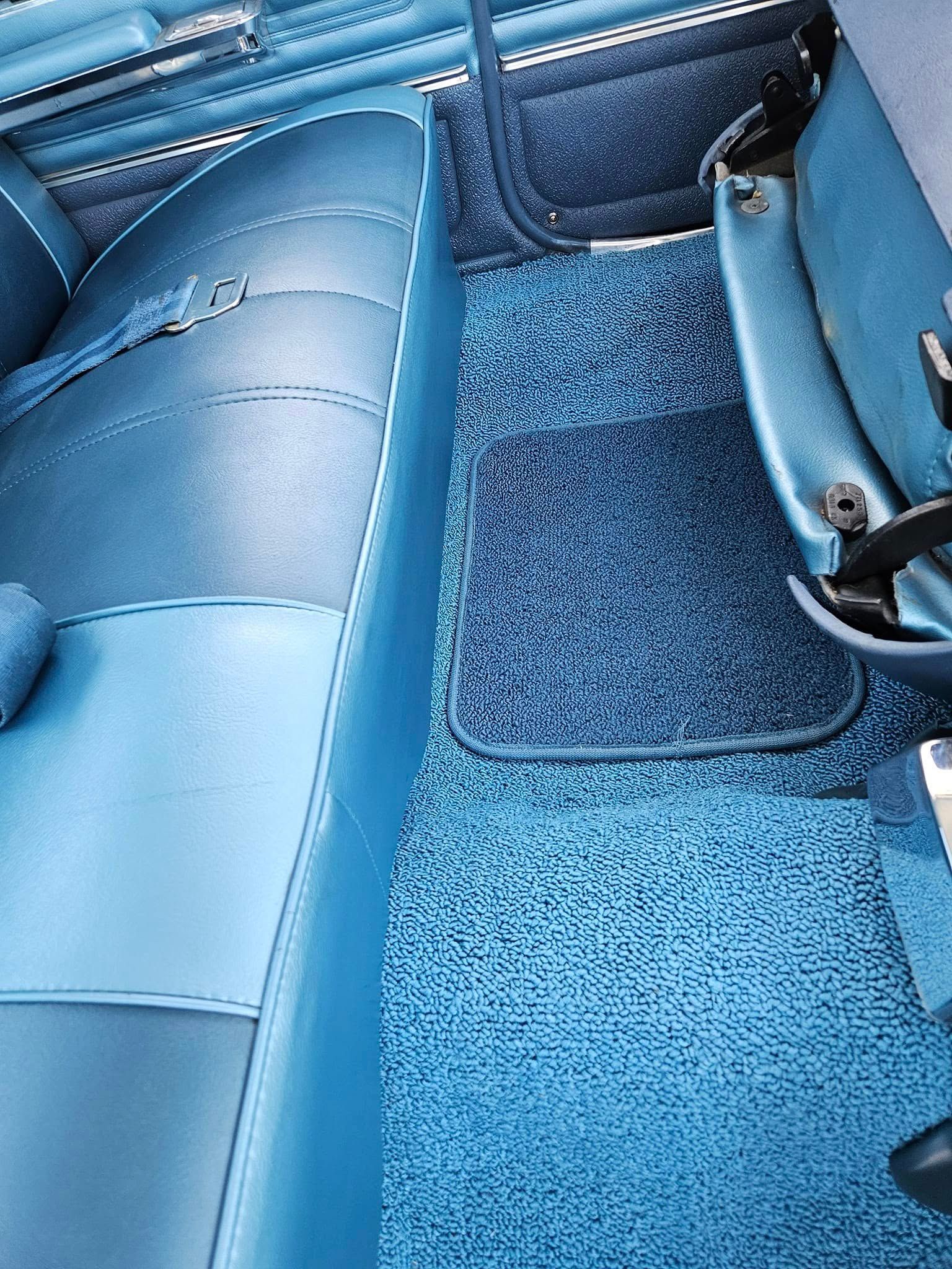 The blue interior of a vintage car, showing a bench seat, textured carpeting, and a matching floor mat.