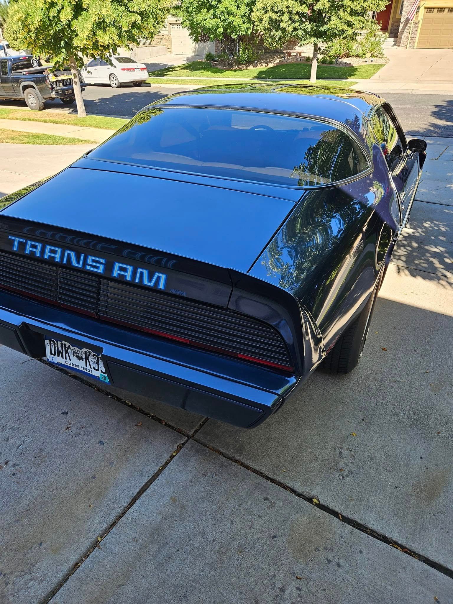 A dark blue Pontiac Trans Am parked on a concrete driveway with a suburban neighborhood in the background.