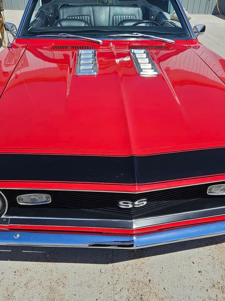 A bright red vintage Chevrolet Camaro SS convertible, viewed from the front, parked on concrete.