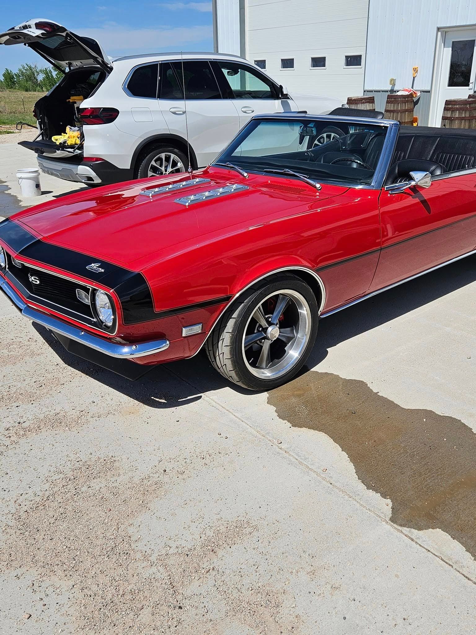 A bright red vintage convertible parked next to a modern white SUV on a sunny day.
