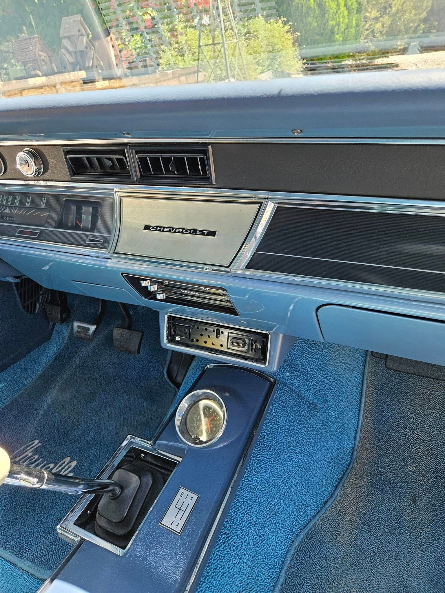 Interior view of a vintage blue car dashboard with a center console, gear shifter, and textured blue carpeting.