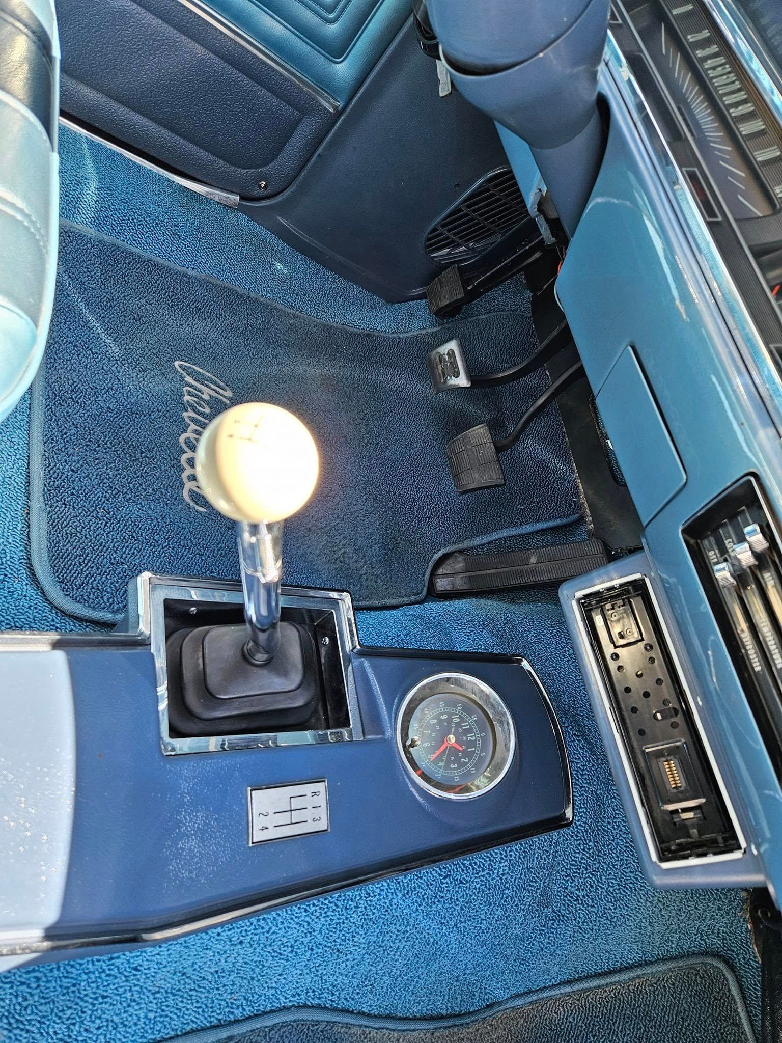A blue classic car interior featuring a manual gear shifter with a round white knob and a circular gauge on the console.