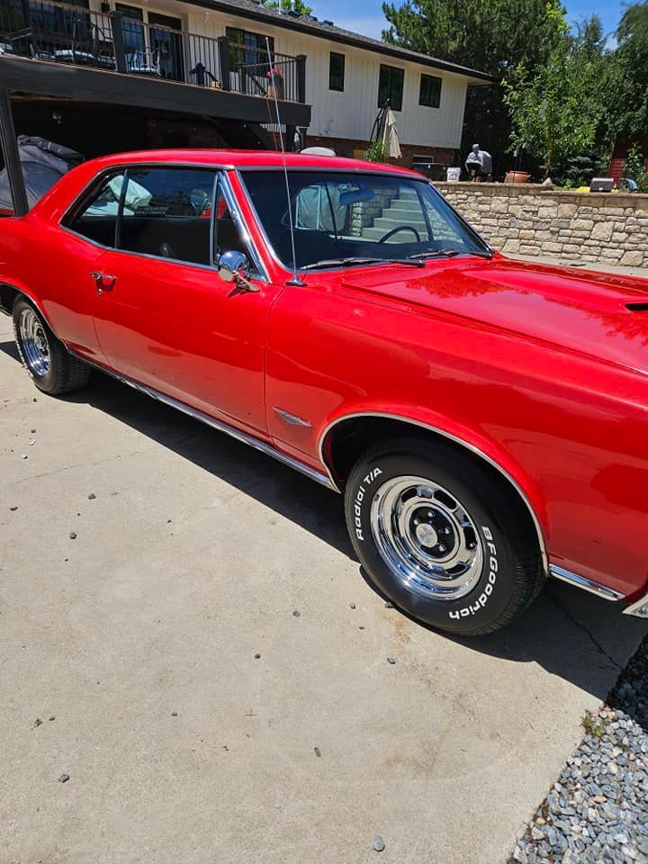 A bright red vintage muscle car parked on a concrete driveway in front of a house.