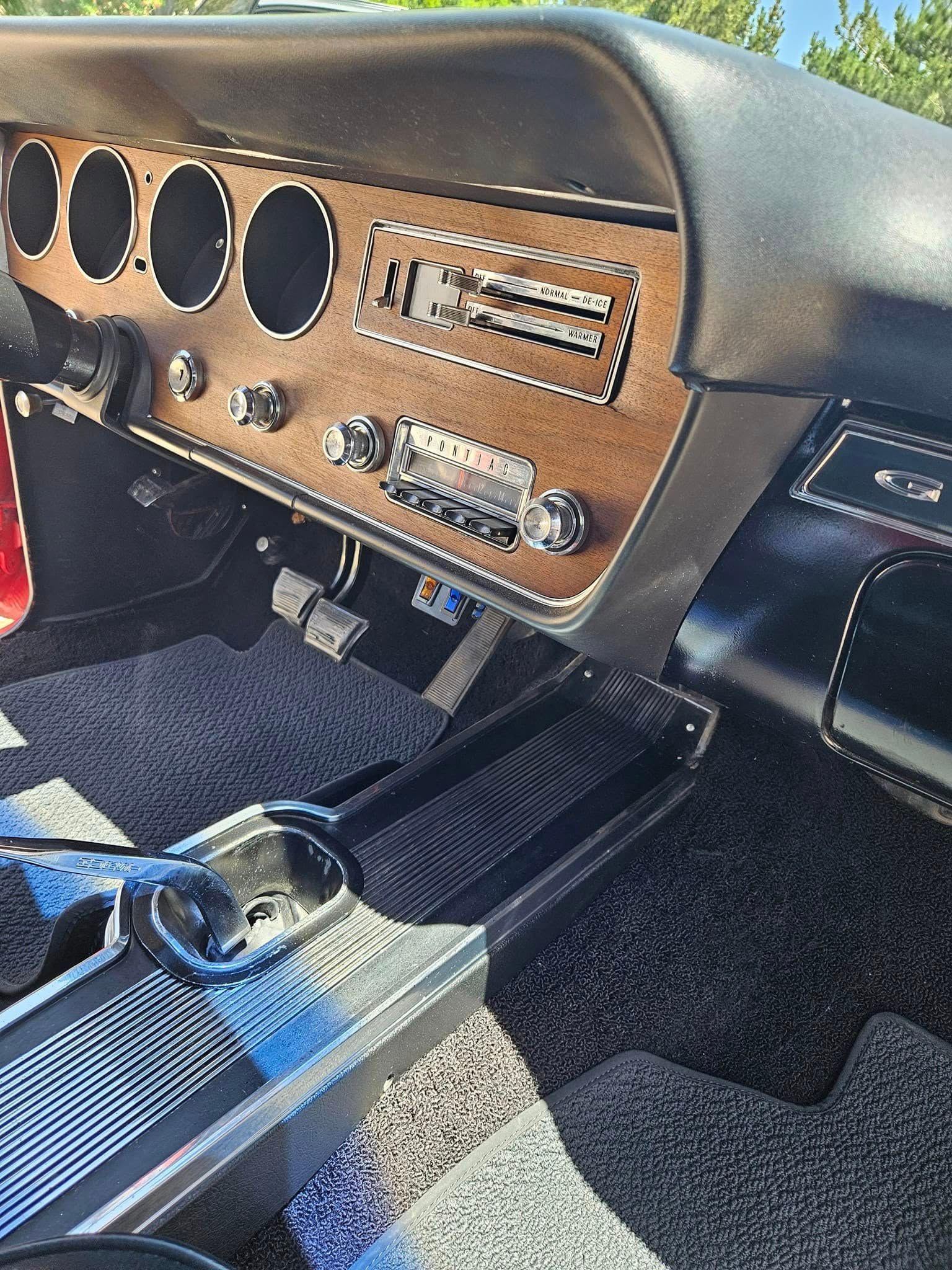 The driver’s side interior of a classic car with a wood-grain dashboard, black steering wheel, and center console.