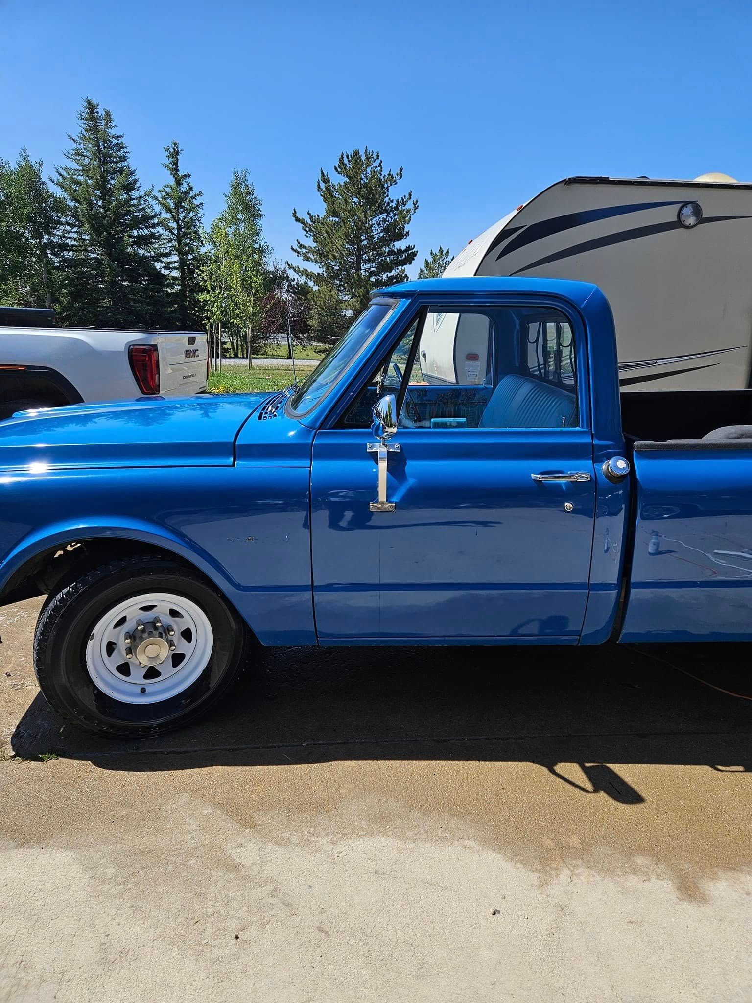 A bright blue vintage Chevrolet C10 pickup truck parked outdoors on a sunny day next to a camper trailer.