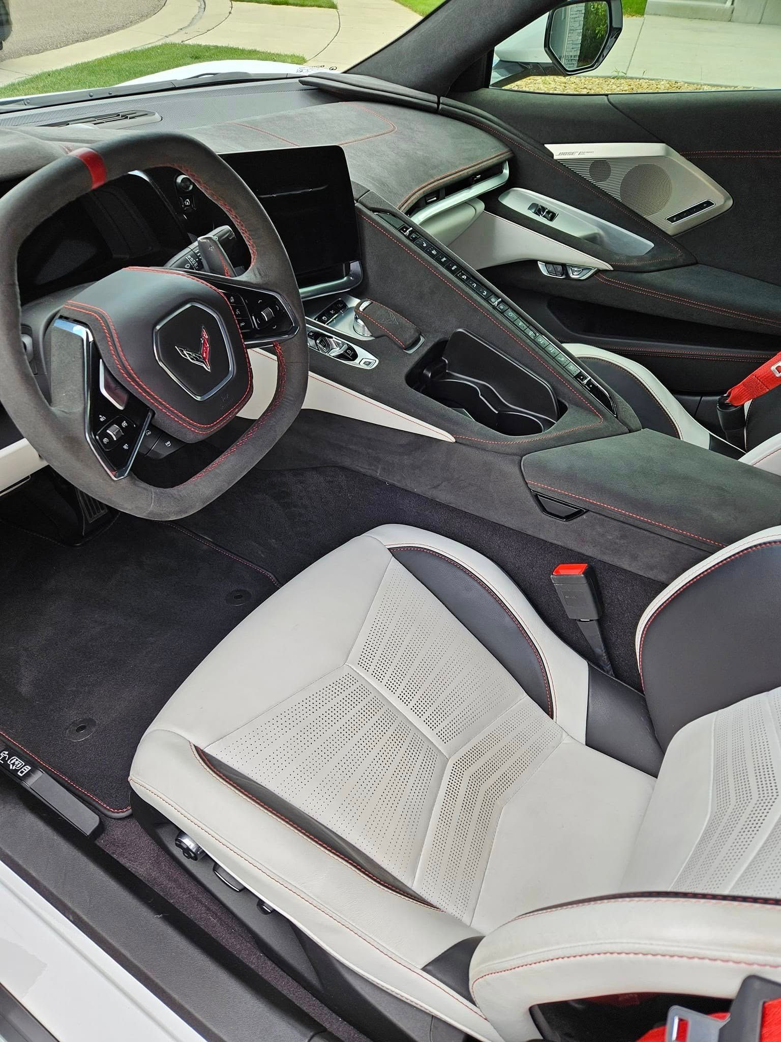 Interior view of a modern sports car featuring a grey and white leather driver's seat, steering wheel, and dashboard.