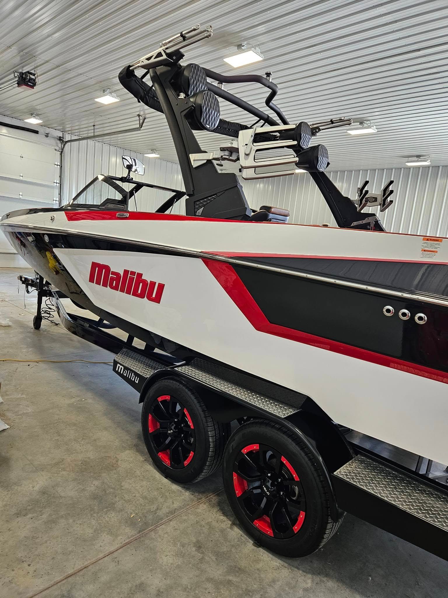 A white and black Malibu ski boat with red accents on a double-axle trailer in a garage.
