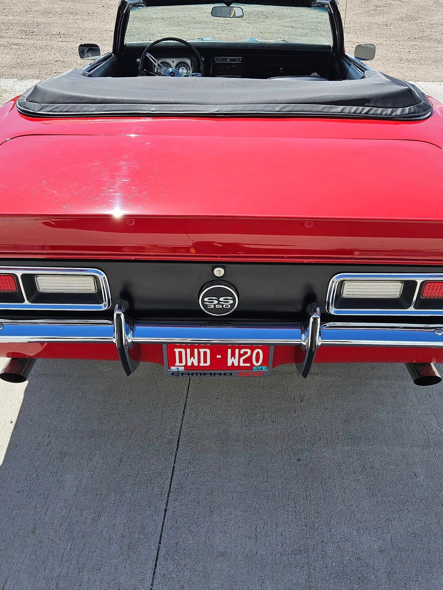 Rear view of a red convertible car with a black trunk panel, chrome bumper, and a license plate reading DND-W20.