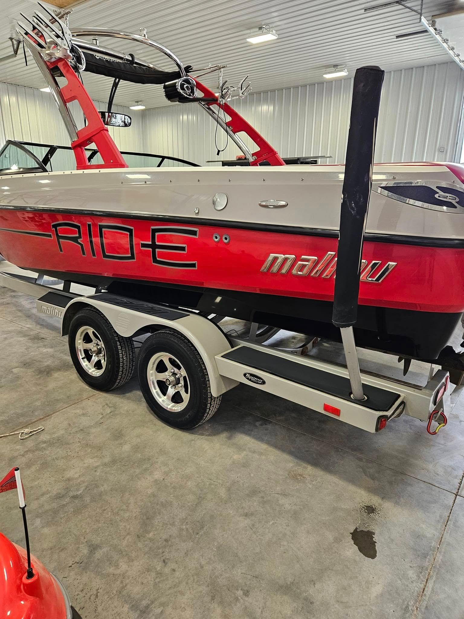 A red and gray Malibu boat on a dual-axle trailer inside a warehouse.