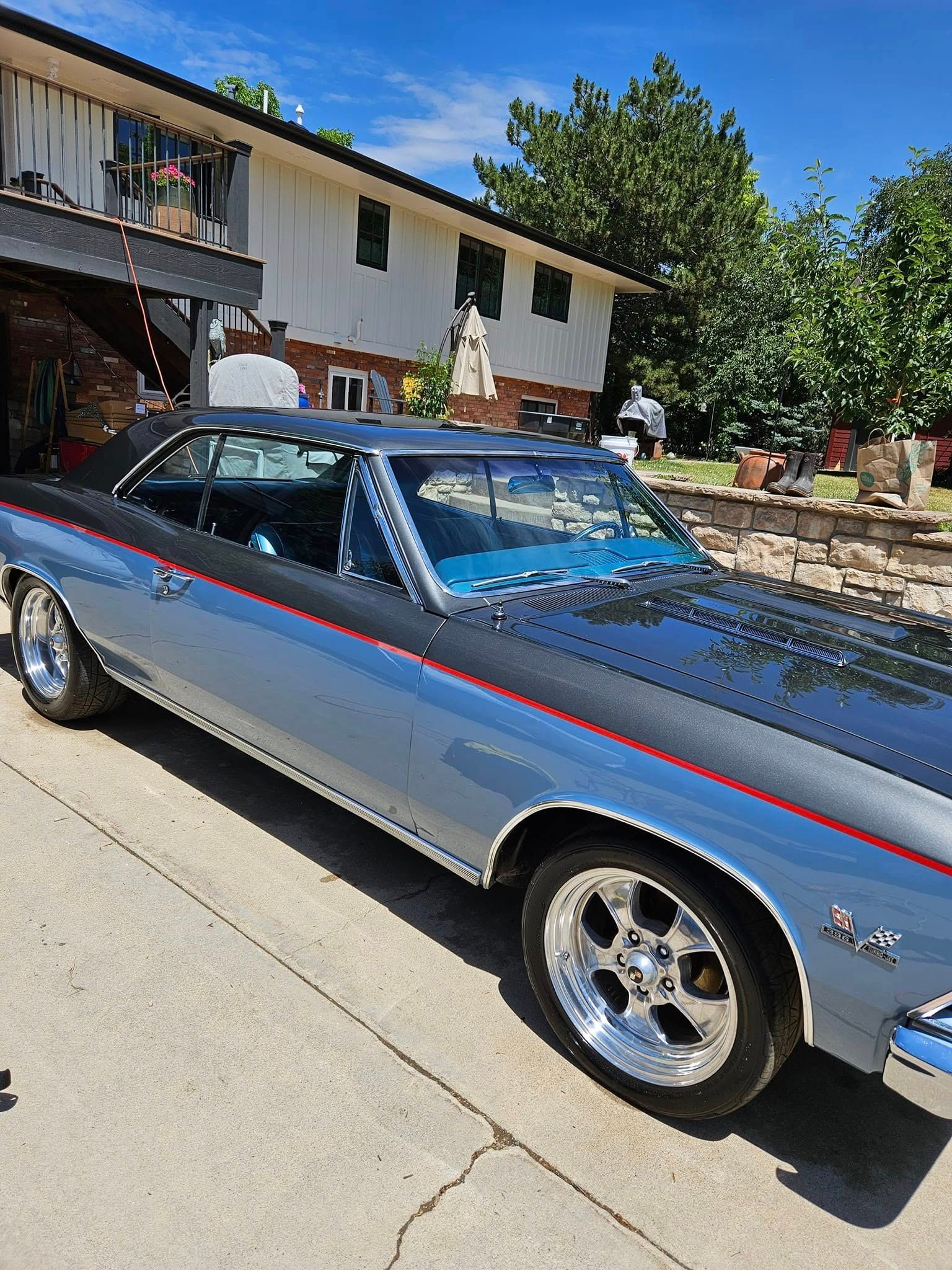 A two-tone silver and dark gray classic Chevrolet muscle car parked on a concrete driveway in front of a house.