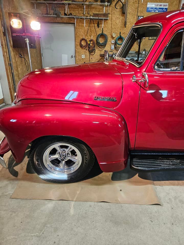 A glossy red vintage Chevrolet pickup truck parked in a well-lit workshop with tools on the wall.