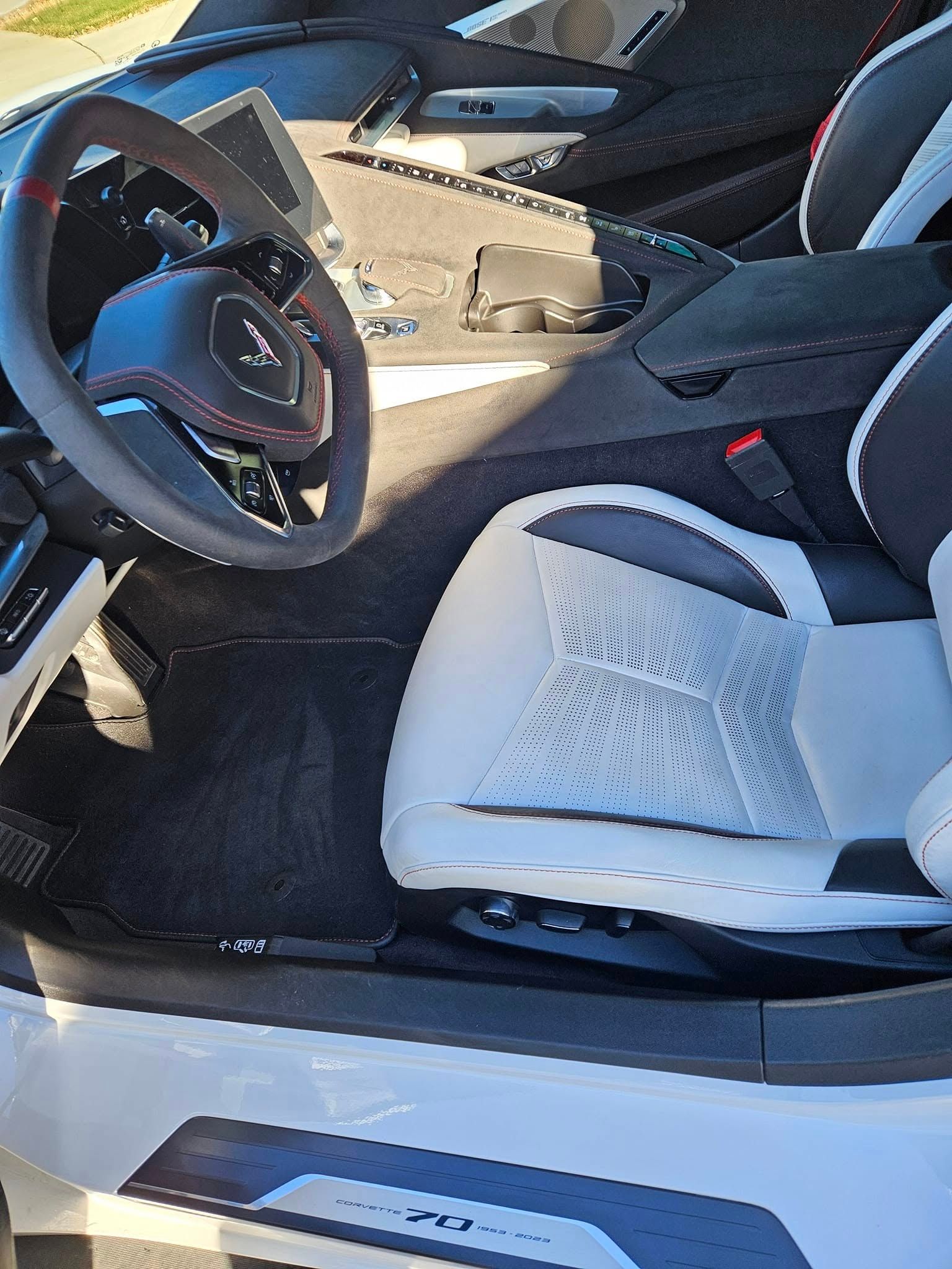 A high-angle view of a white and black modern car interior, showing the steering wheel, console, and driver's seat.
