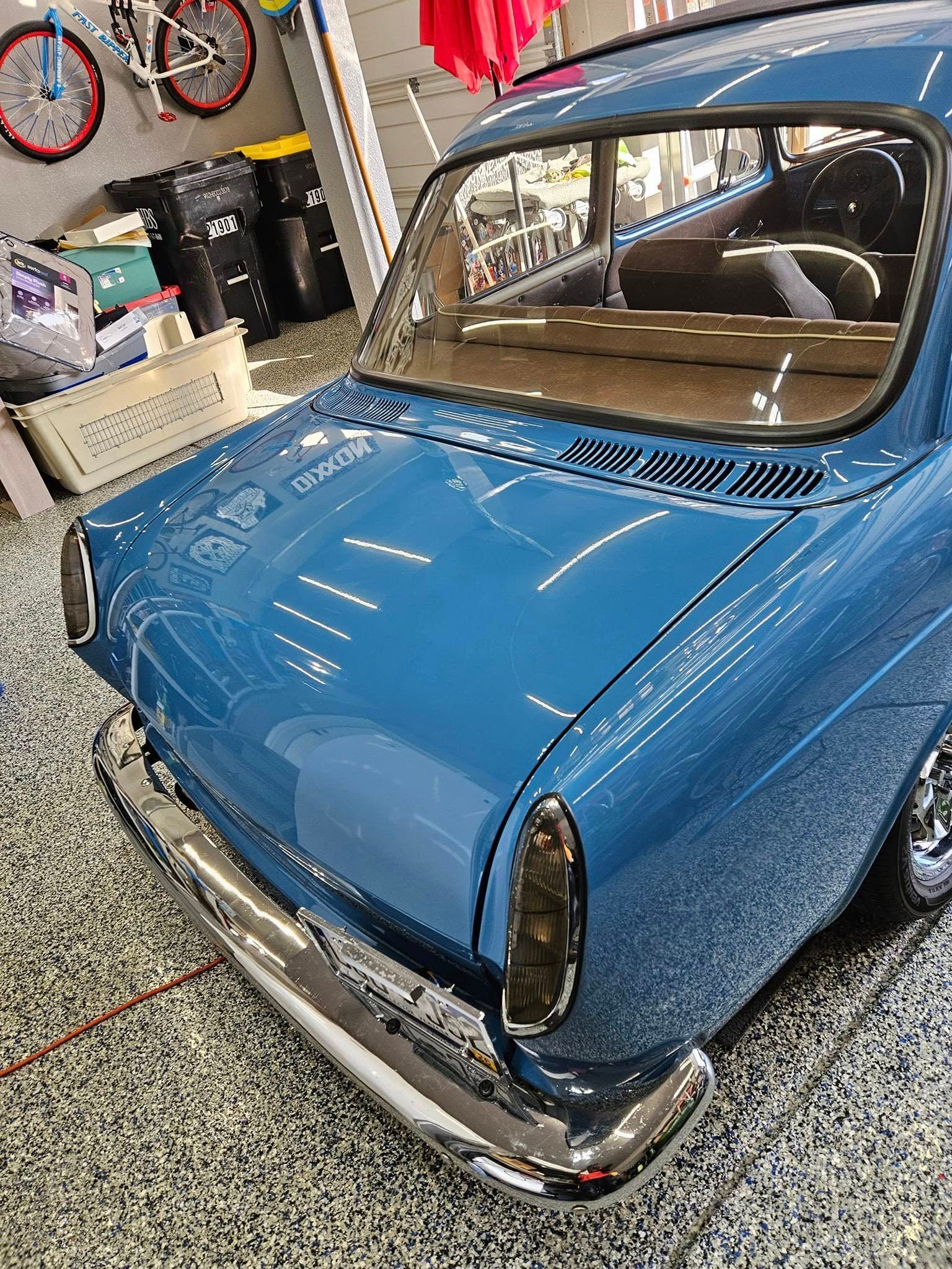 Rear angle of a glossy blue vintage Volkswagen Type 3 sedan parked inside a garage with a bicycle hanging on the wall.