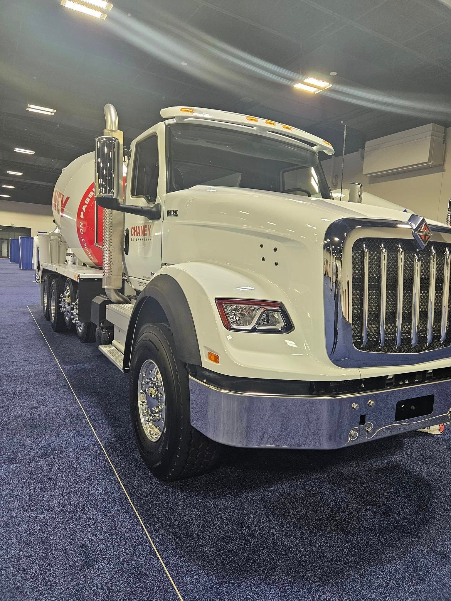 A white International truck with a concrete mixer tank parked on a blue carpet in an indoor event space.