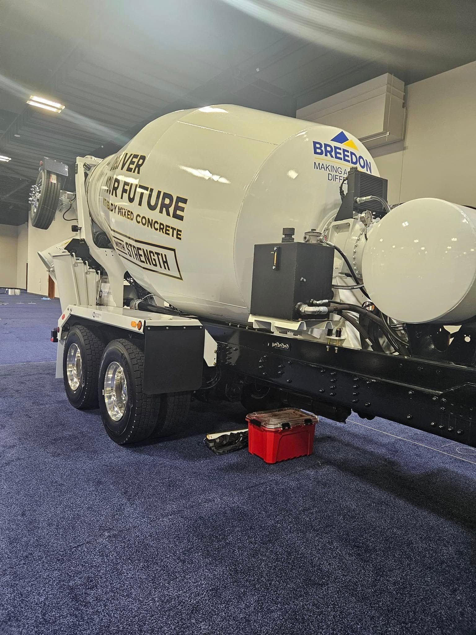 A white Breez-E concrete mixer trailer parked indoors on a blue carpeted floor.