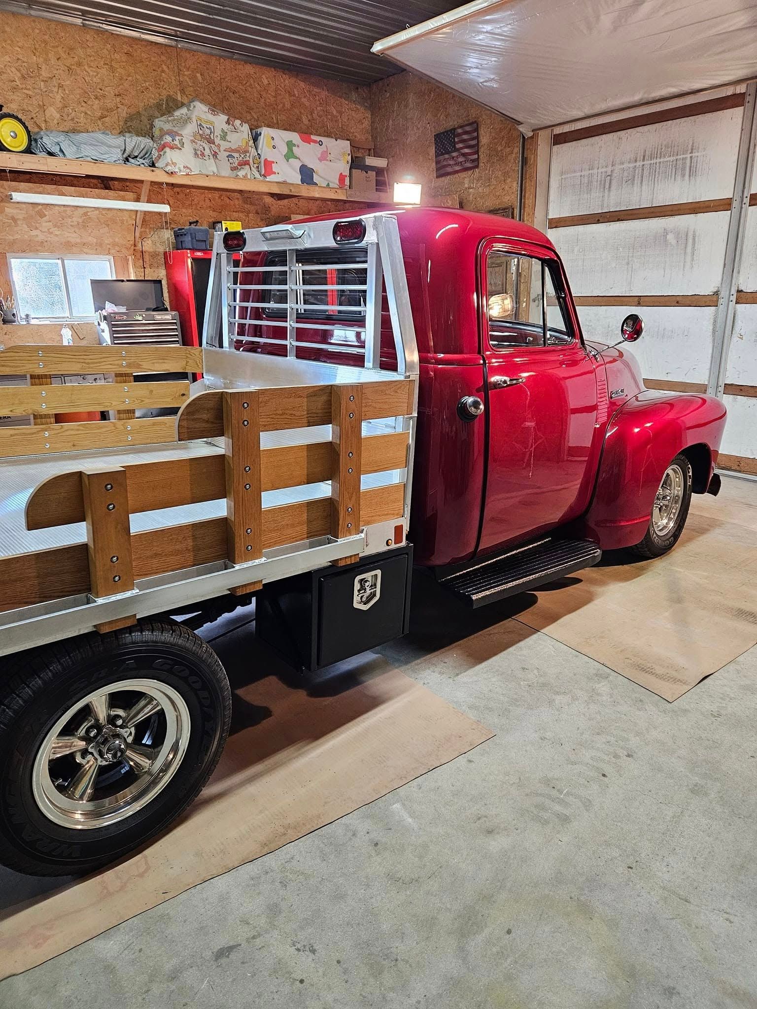 A glossy red vintage truck with a flatbed and wooden sides parked inside a workshop.