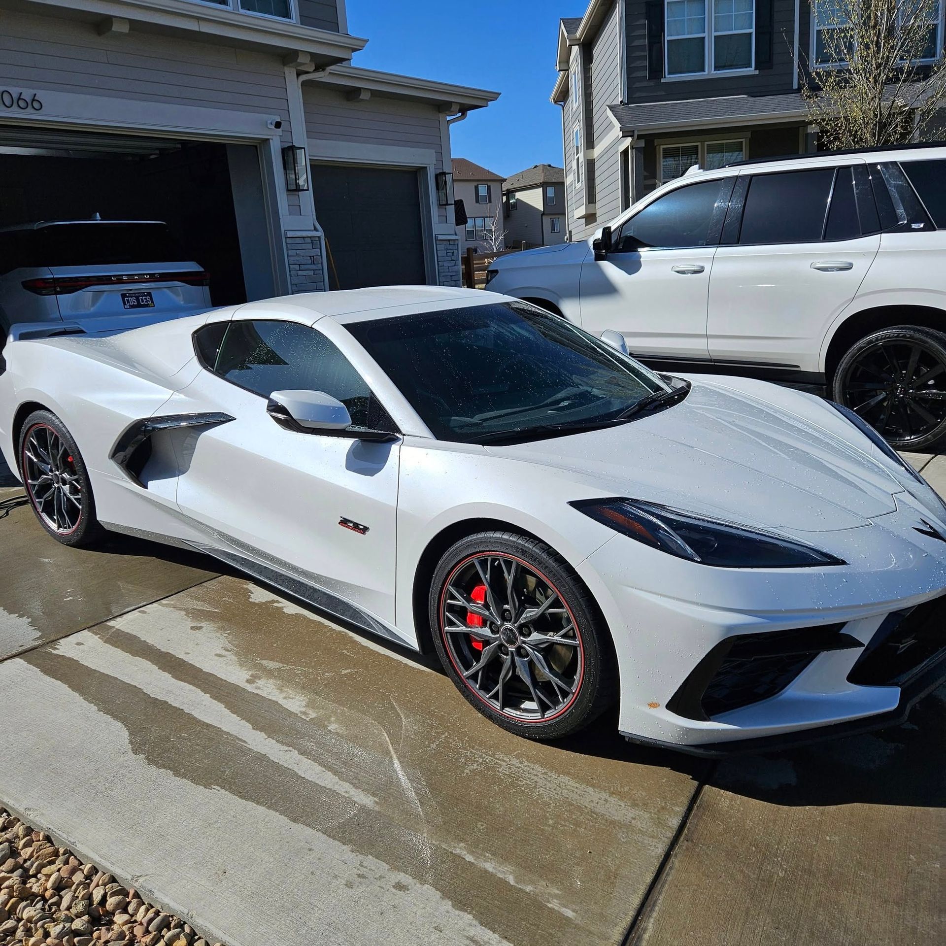 A white Chevrolet Corvette C8 parked in a residential driveway on a sunny day next to a white SUV.