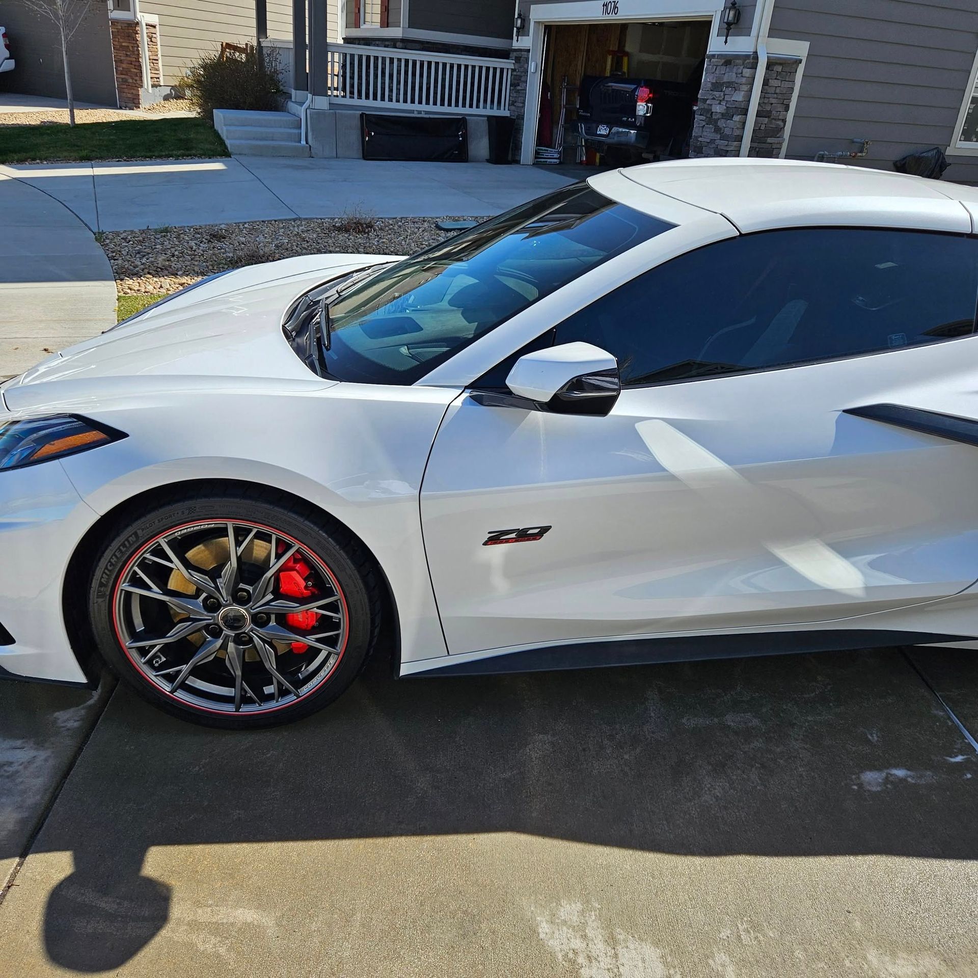 A white Chevrolet Corvette C8 sports car parked on a concrete driveway in front of a house.