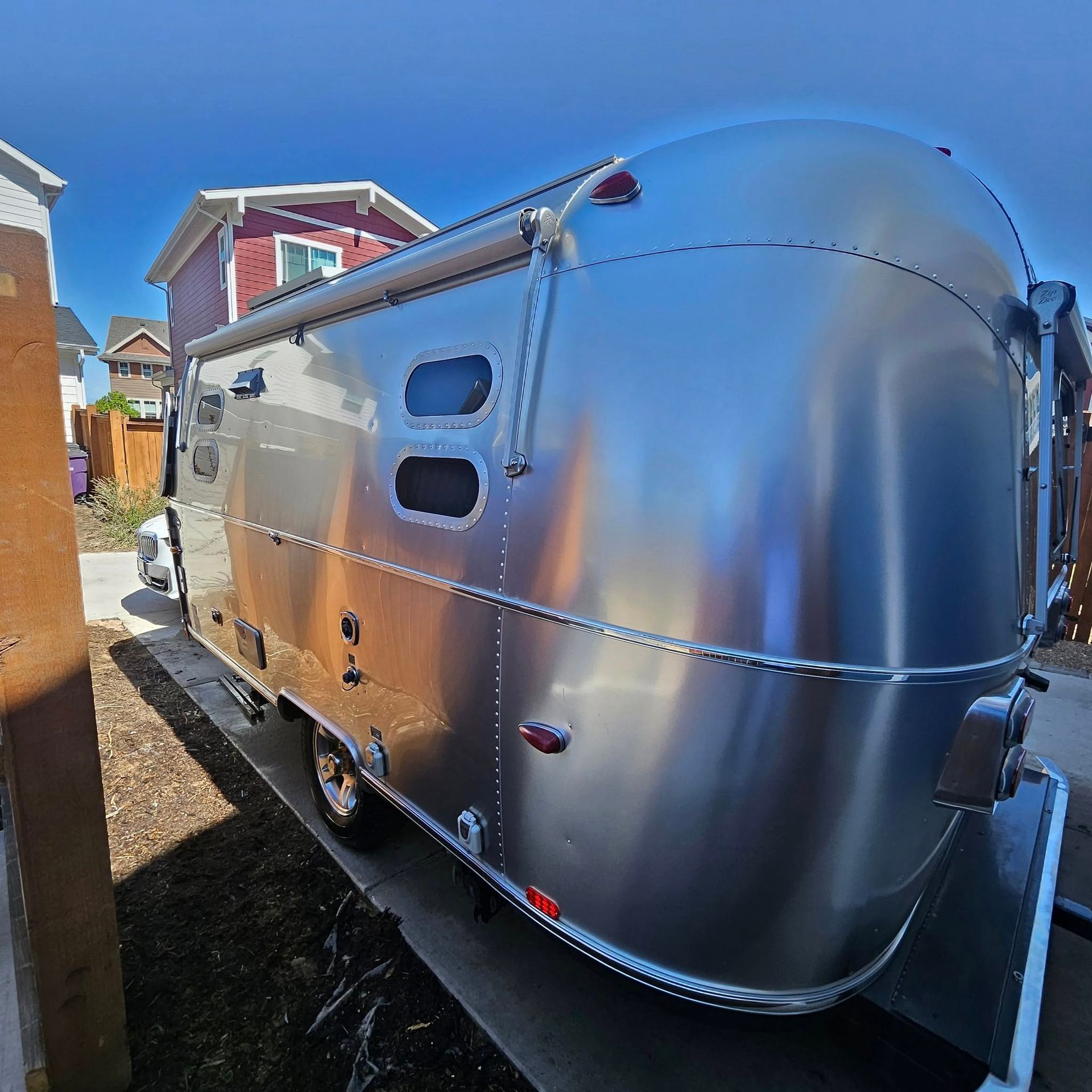 A shiny, silver Airstream travel trailer parked on a concrete driveway next to a wooden fence and a house.