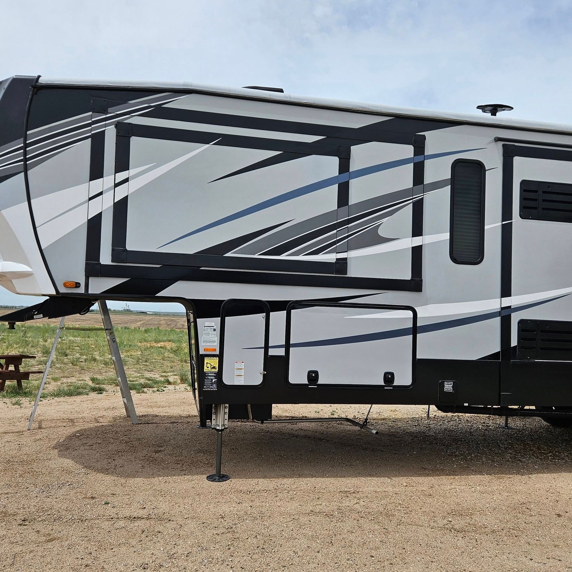 Side view of a grey and black fifth-wheel recreational vehicle parked on gravel.