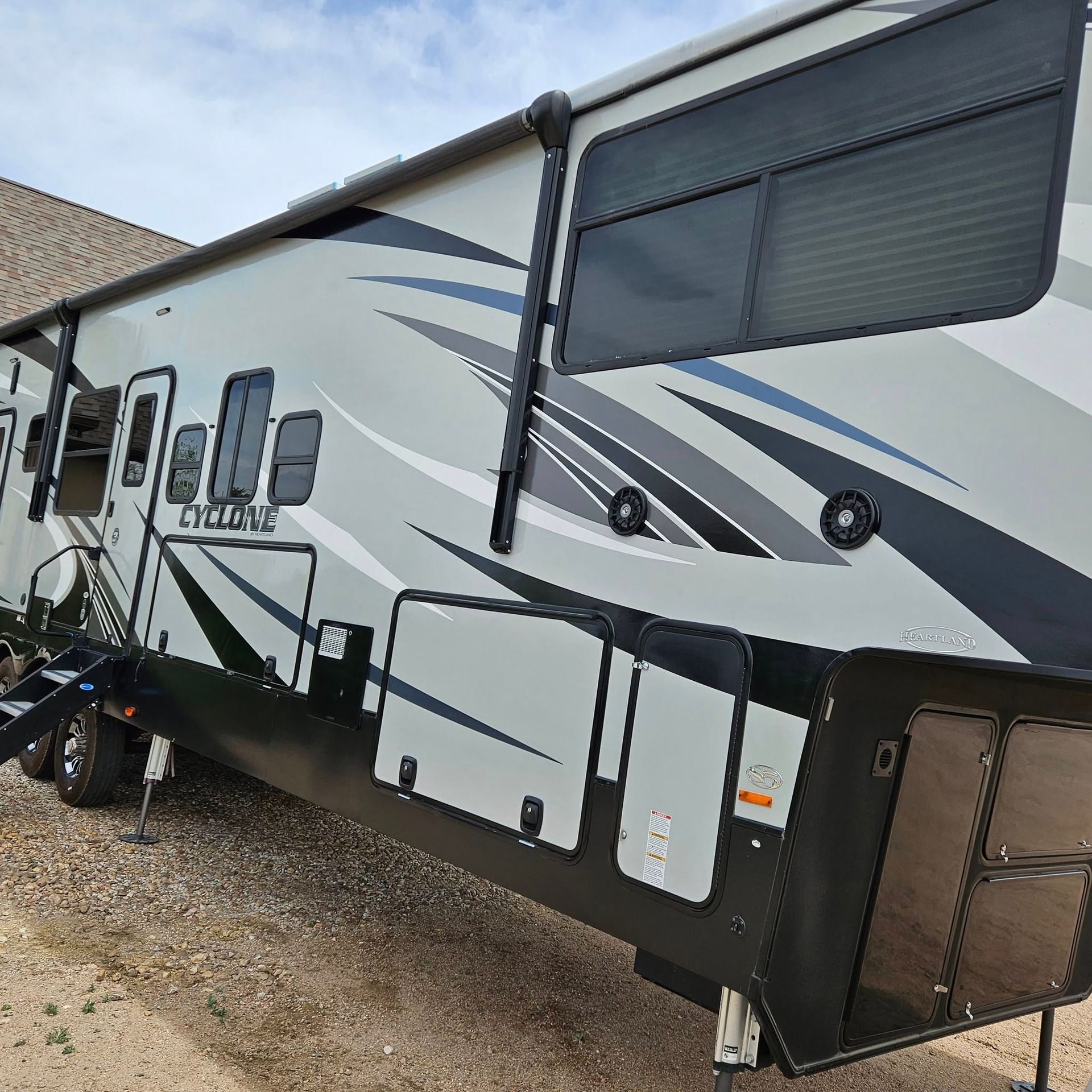 A side view of a grey Heartland Cyclone fifth-wheel toy hauler parked outdoors on gravel.