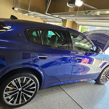 A blue luxury SUV parked in a garage with its hood open, showcasing detailed alloy wheels and a light-colored interior.