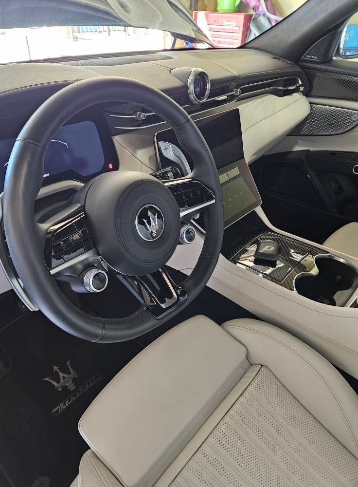 The interior of a Maserati featuring a leather-wrapped steering wheel, digital dashboard, and cream-colored seats.