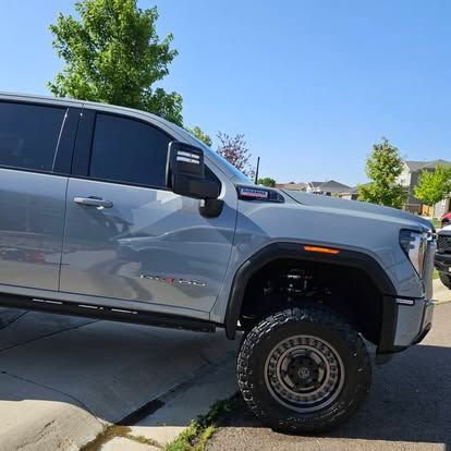 A gray GMC pickup truck with tinted windows and off-road tires parked on a suburban street.